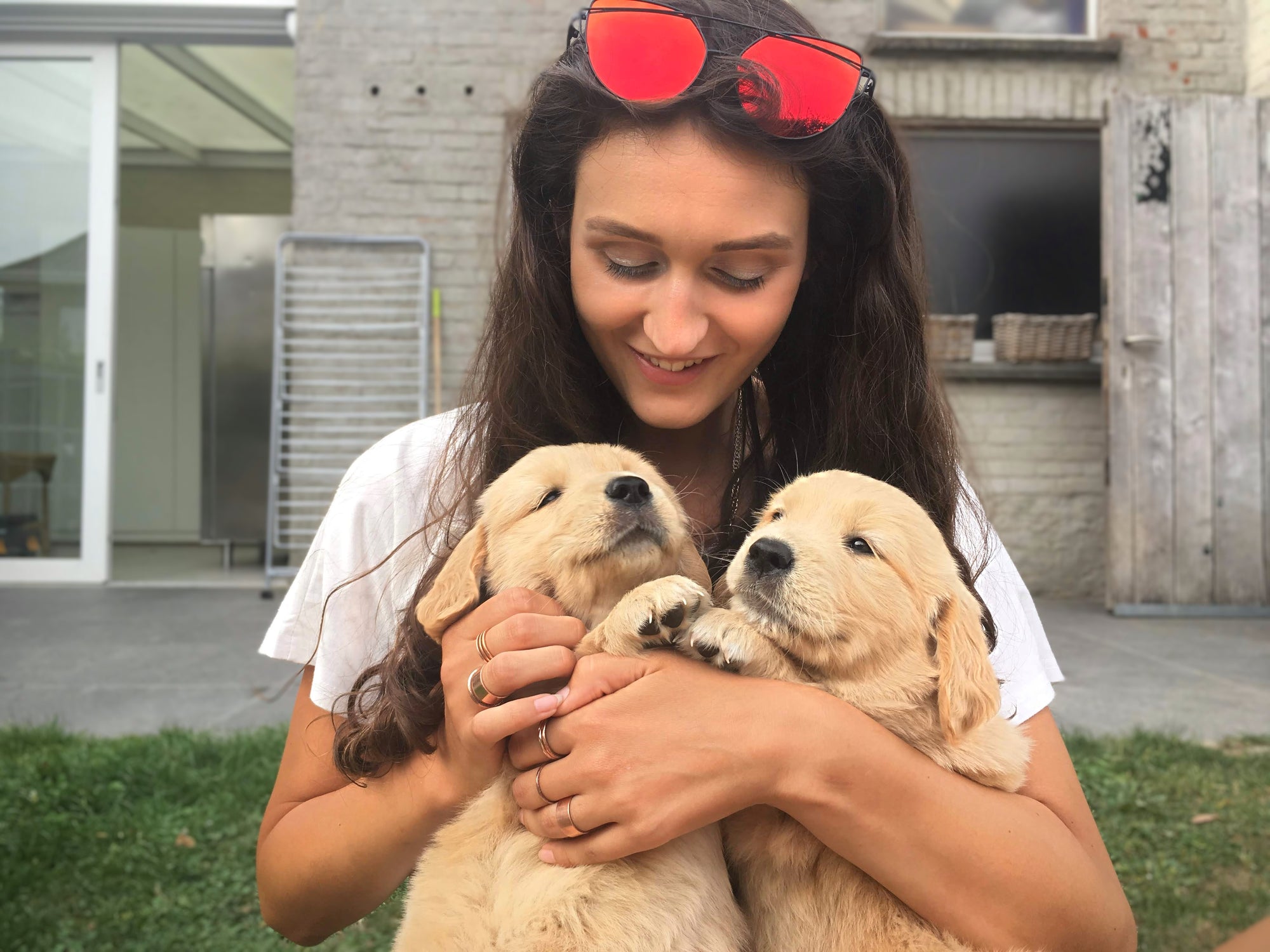 Woman holding two puppies with red sunglasses on her head outdoors.